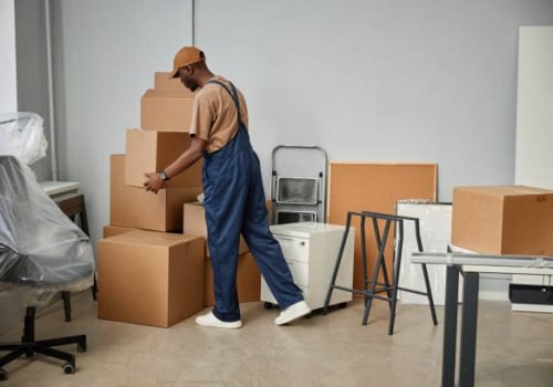 African American loader in uniform carrying boxes in new office